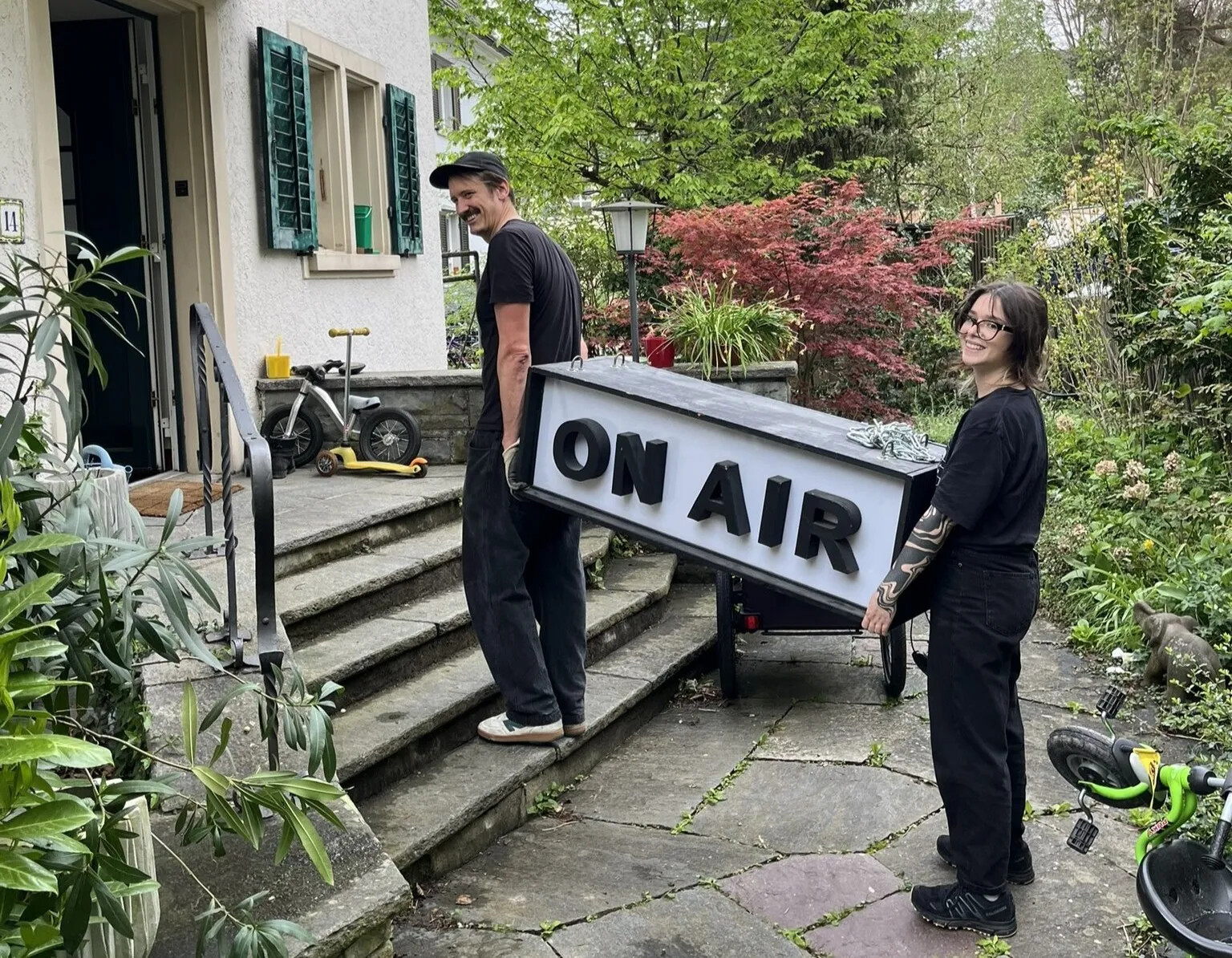 zwei personen tragen ein grosses leuchtschild mit on air schriftzug